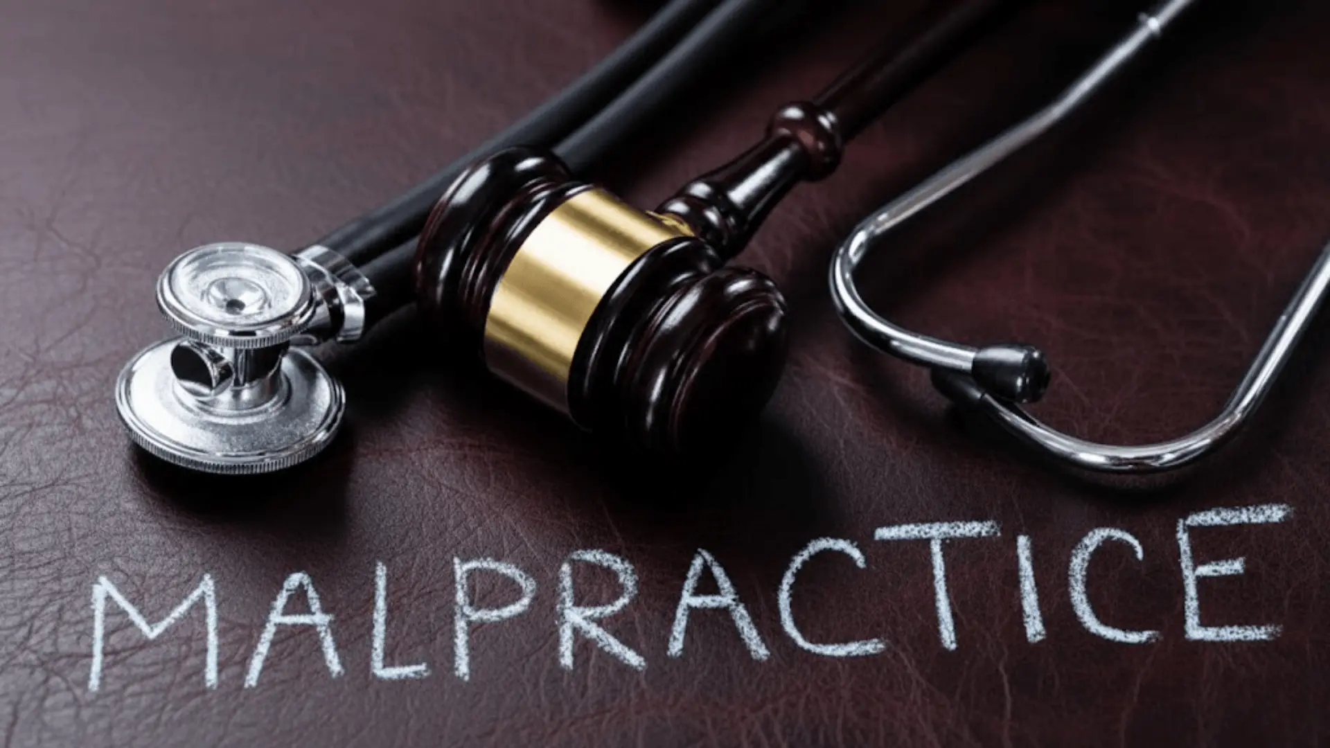 A close-up of a wooden judge's gavel and a medical stethoscope resting on a dark leather surface with the word _MALPRACTICE._