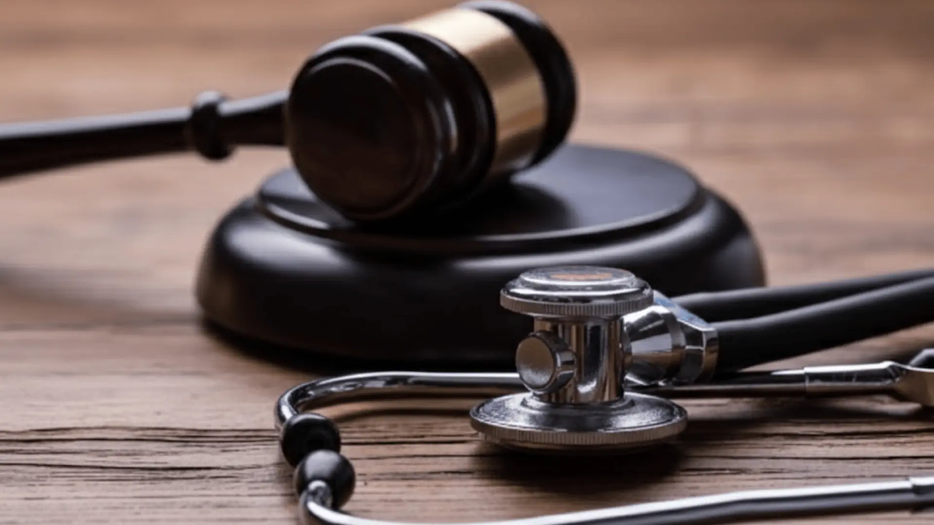 A shallow-depth-of-field shot of a wooden gavel and sound block next to a stethoscope on a rustic wooden table