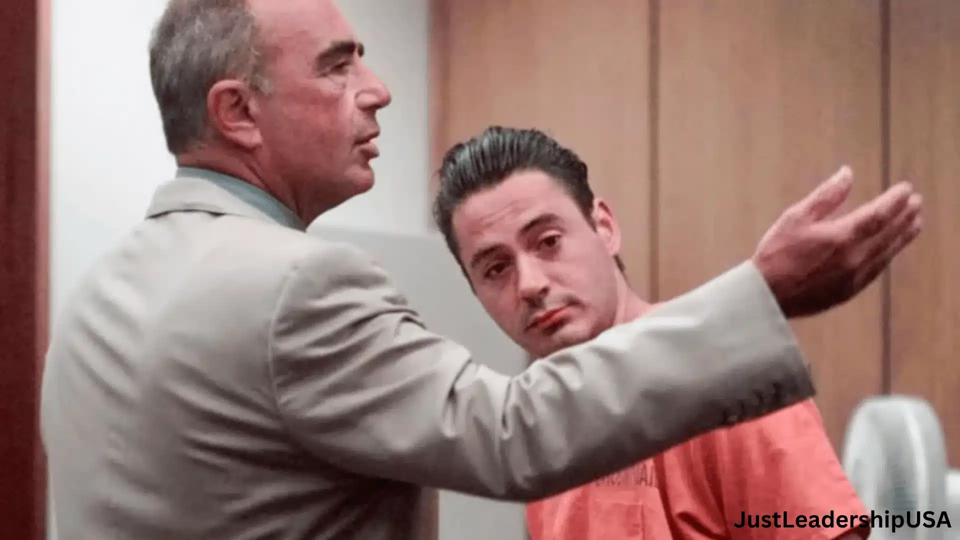 A side profile of Robert Downey Jr. in an orange jumpsuit standing next to a man in a tan suit in a courtroom