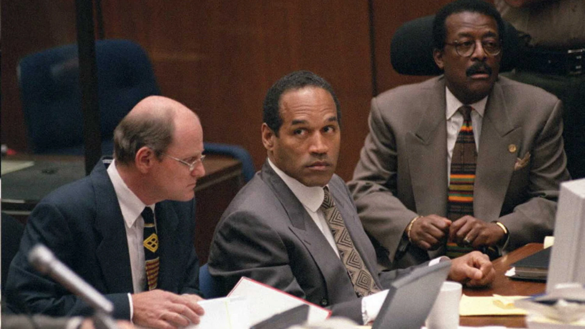 Defendant seated between two attorneys in a courtroom during a high profile 1990s murder trial.