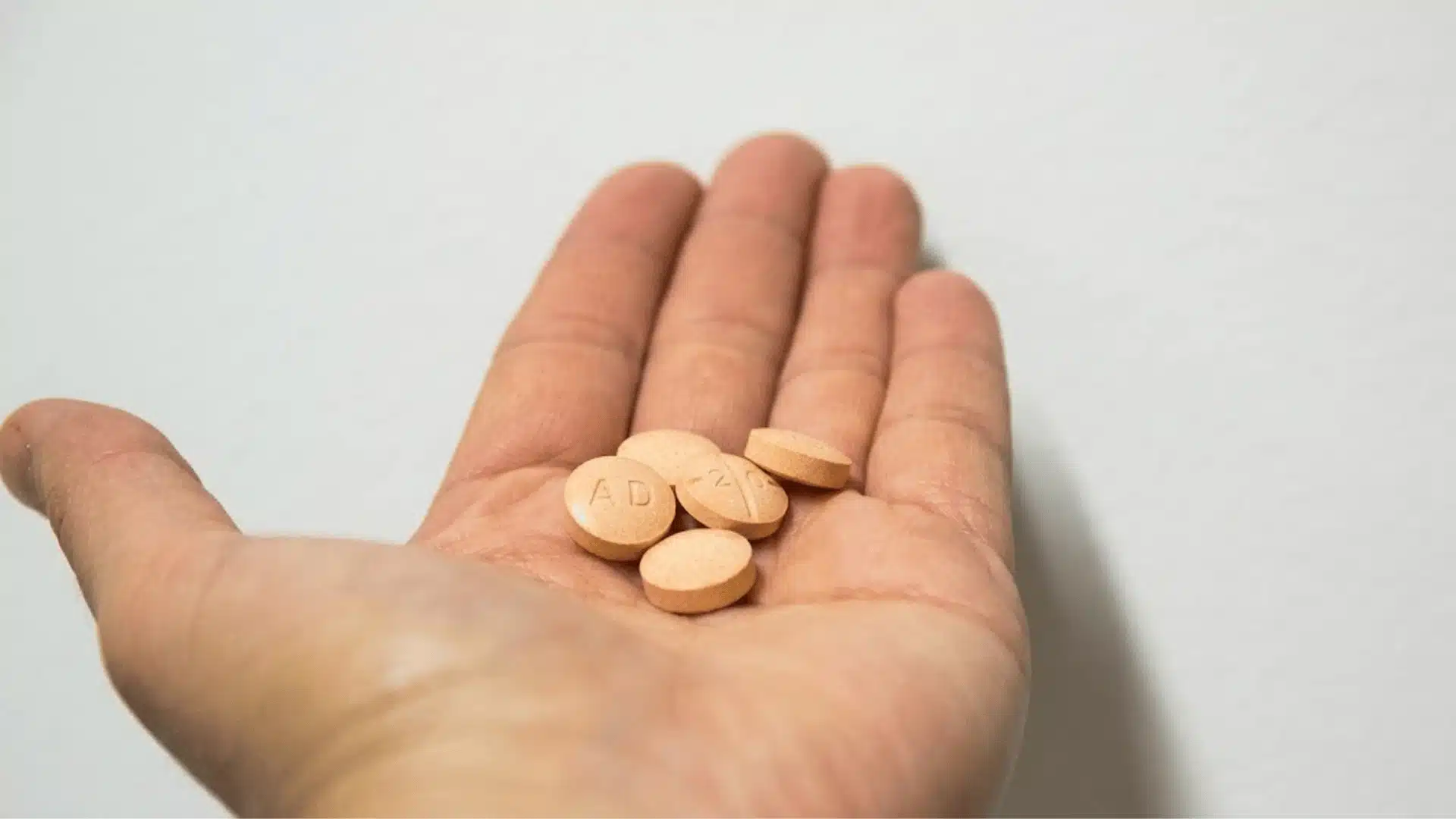 Hand holding orange Adderall tablets with AD and 20 imprint visible on round pills