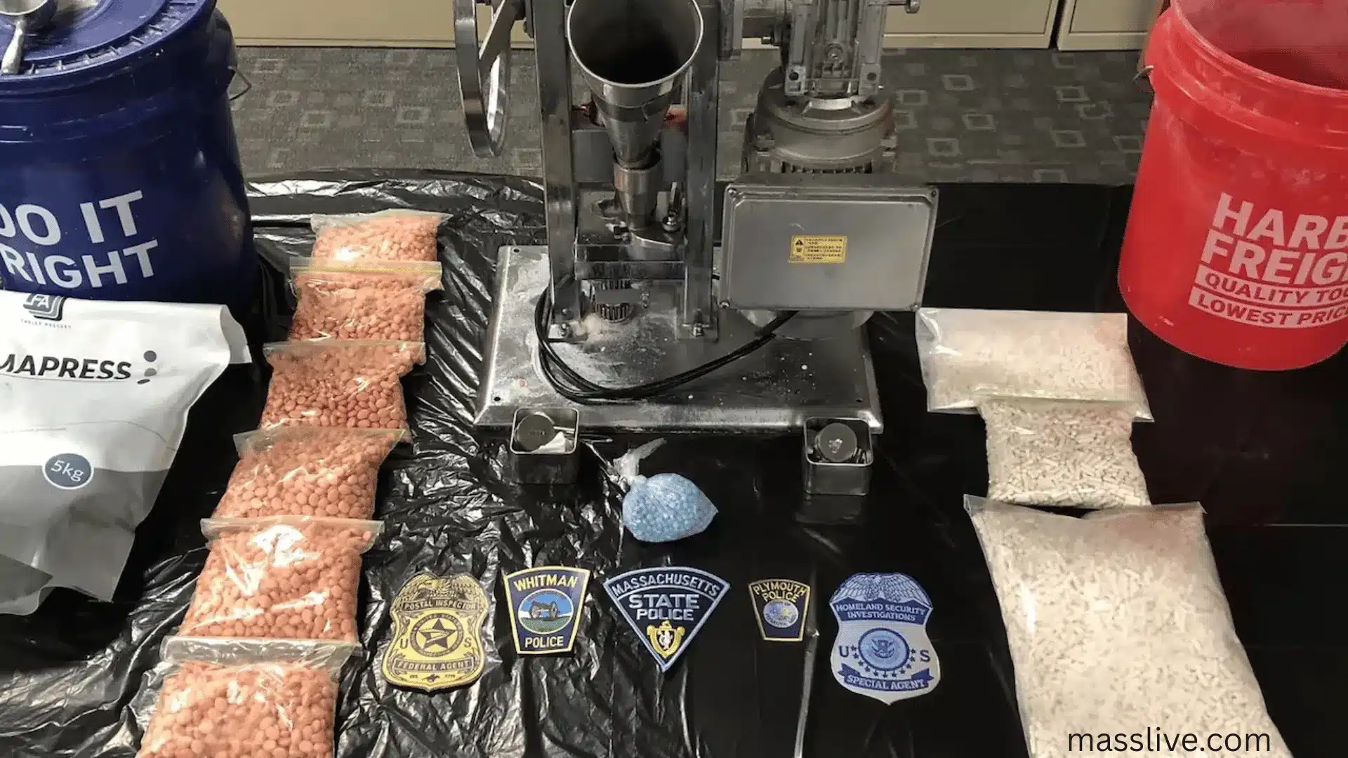Law enforcement display of pill press machine, bags of fake pills, and drug packaging seized in fentanyl bust