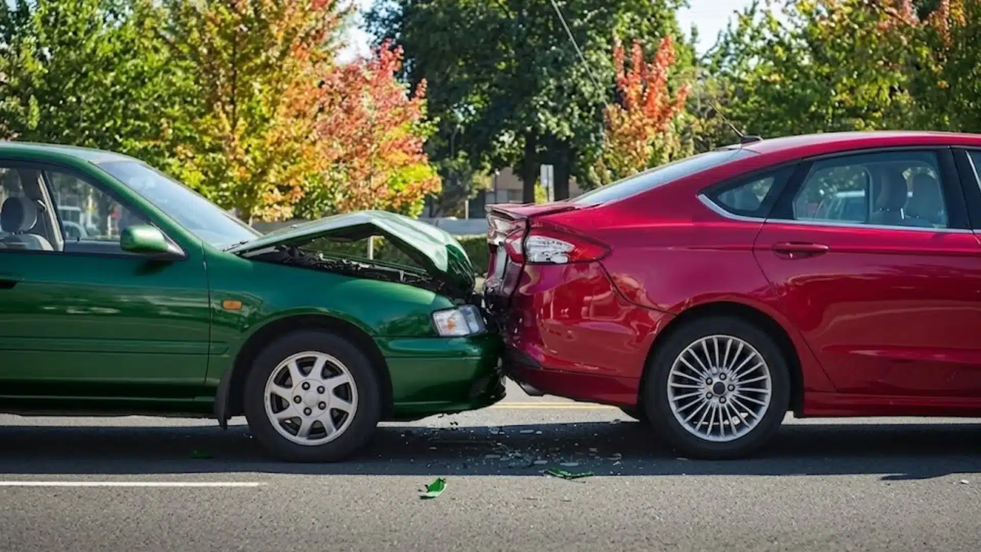 Rear end car accident showing green car hitting red sedan with visible damage on a city street in daylight