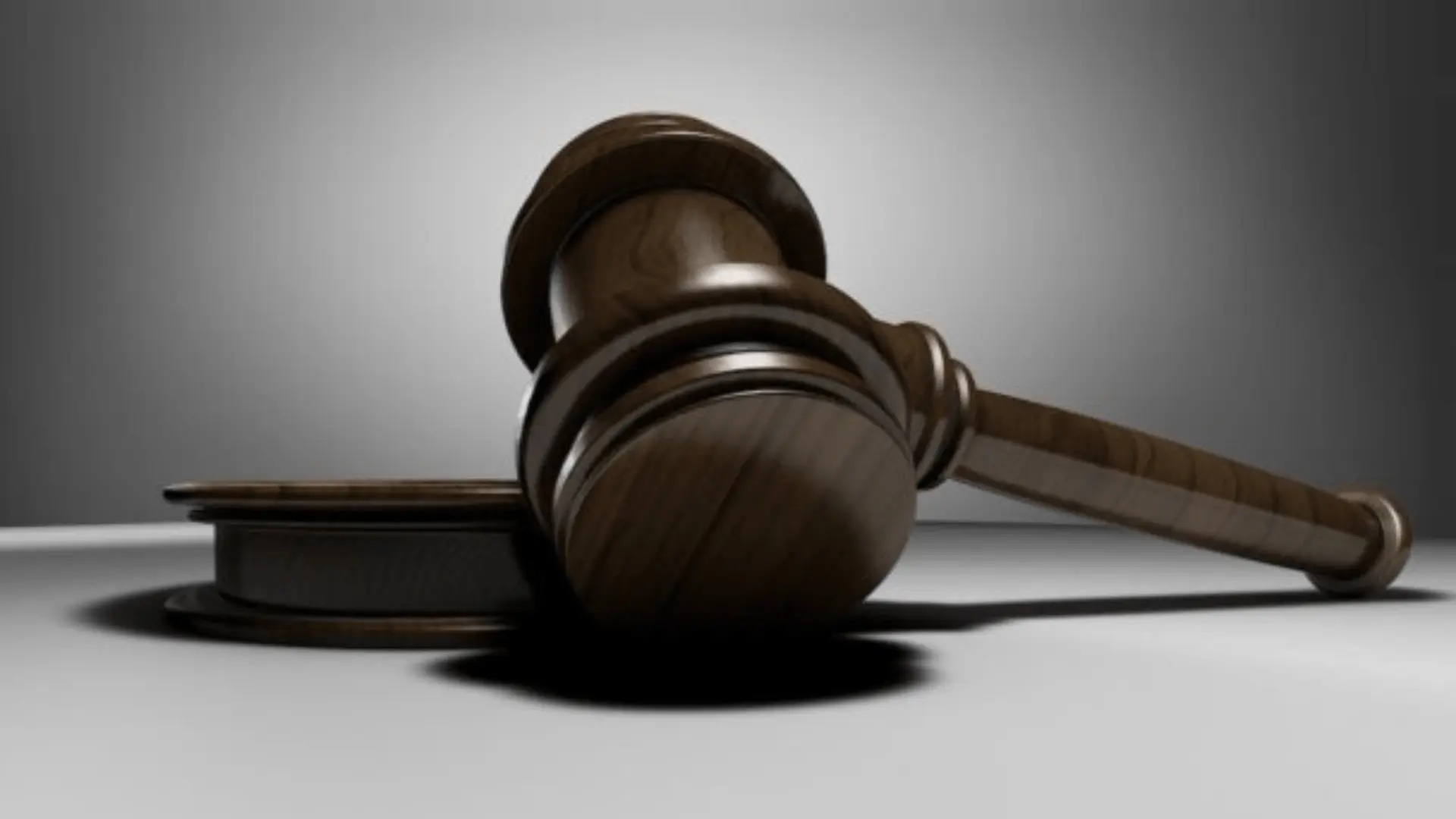 Wooden gavel and block on a surface, spotlighted dramatically against a gradient grey background, conveying a sense of justice and authority