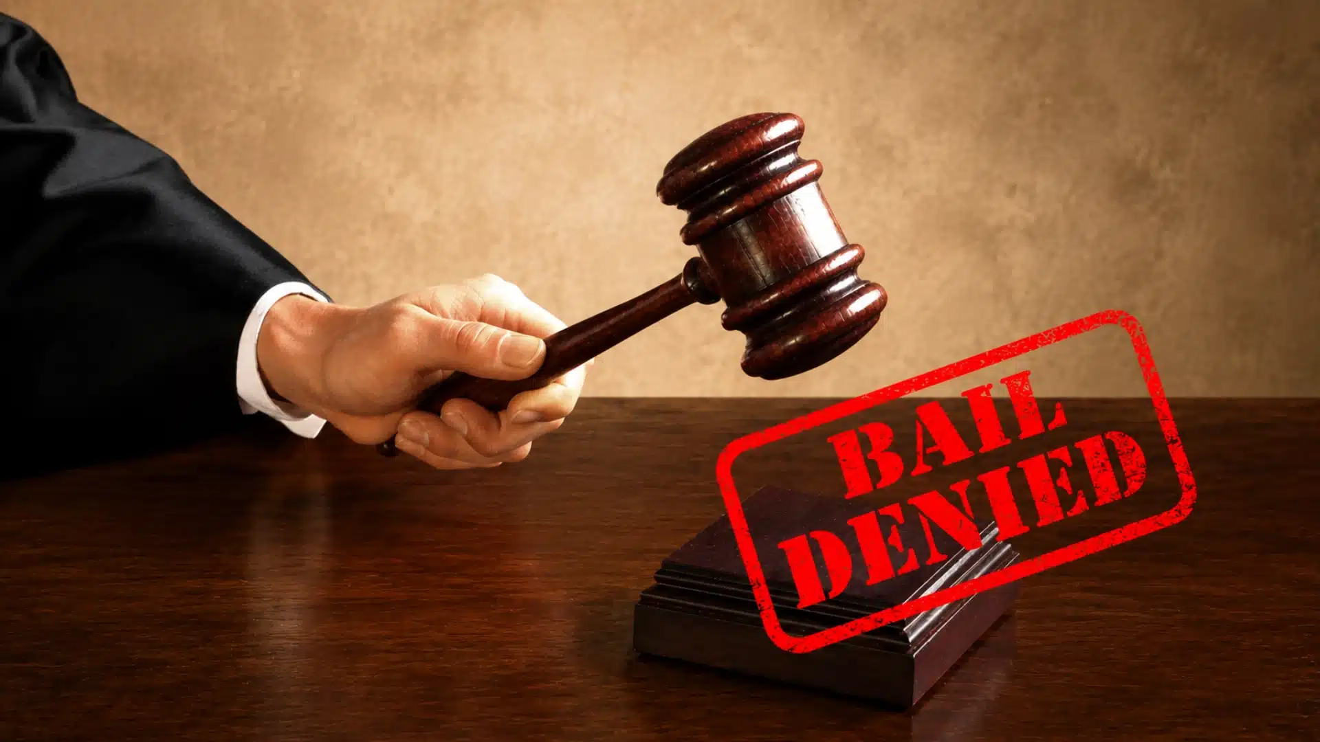 A judge's hand holding a wooden gavel over a sound block with a red _BAIL DENIED_ stamp overlaid