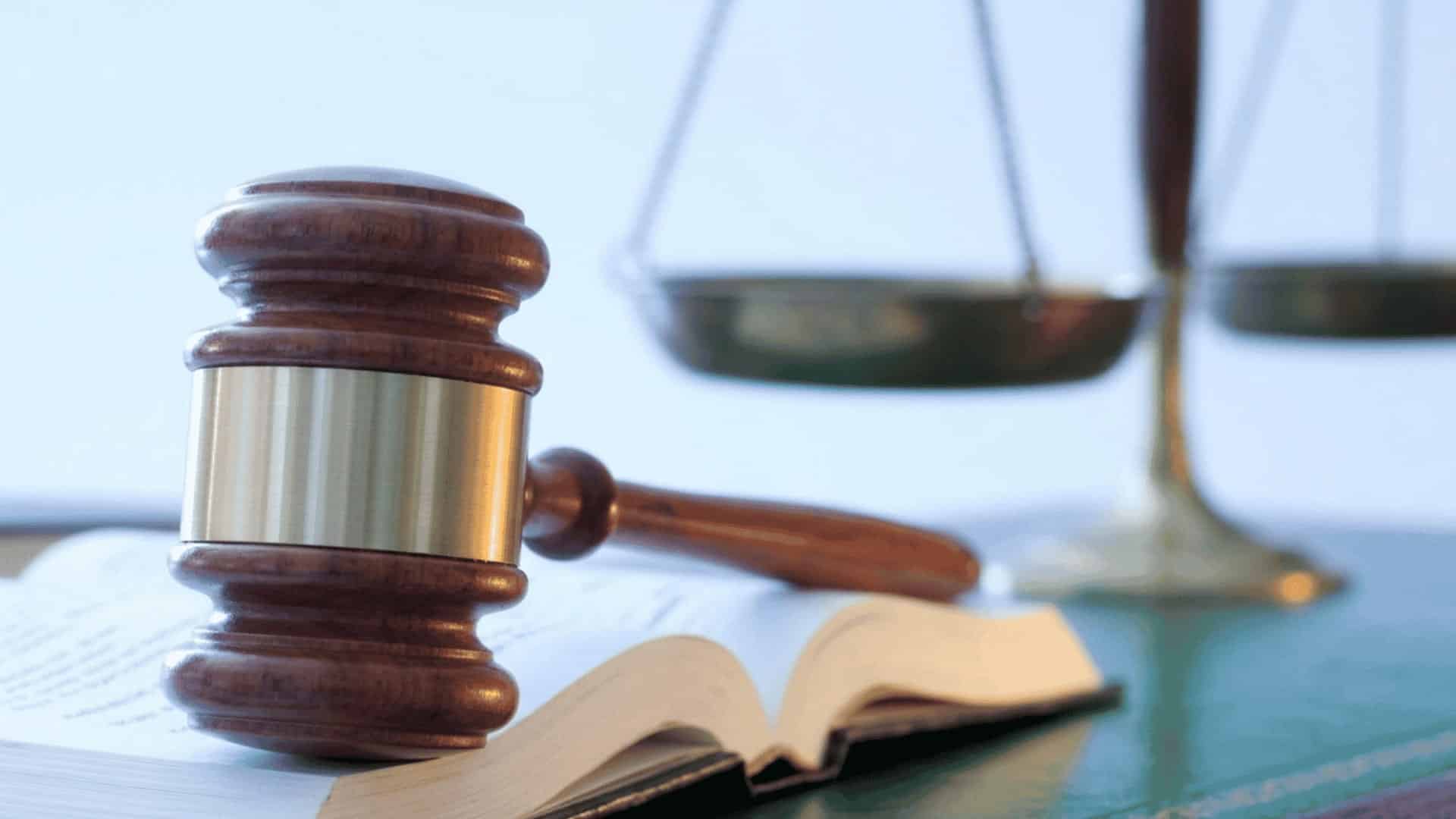 A wooden gavel on an open law book with scales of justice in the background