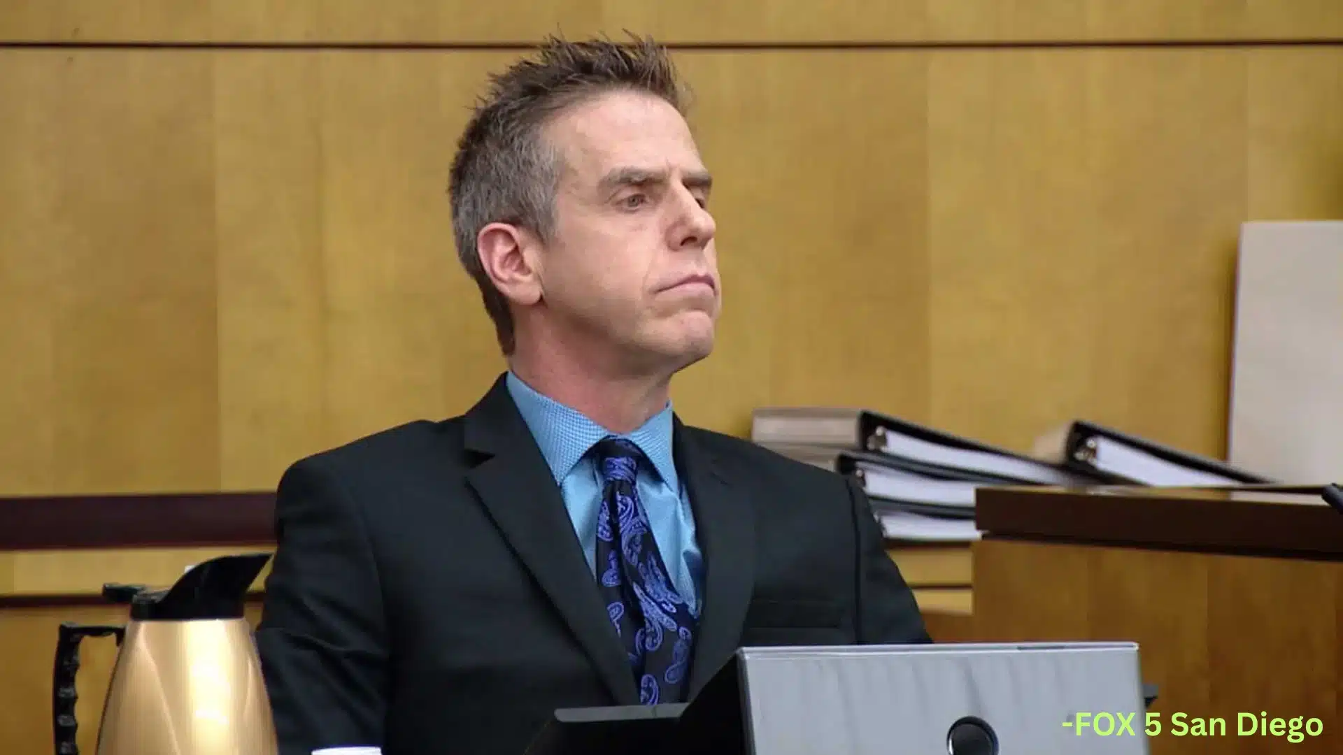 Adam Shacknai seated in a courtroom wearing a dark suit and blue tie during civil court proceedings