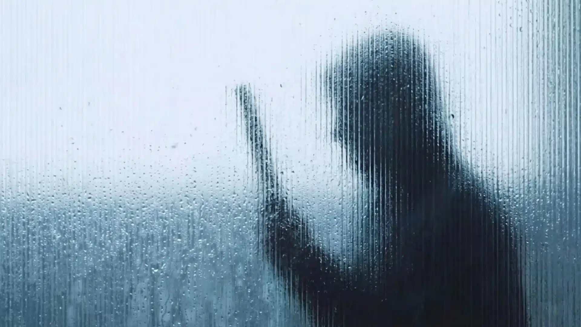 Blurred silhouette of a person holding a knife behind rain-streaked glass in a tense crime scene