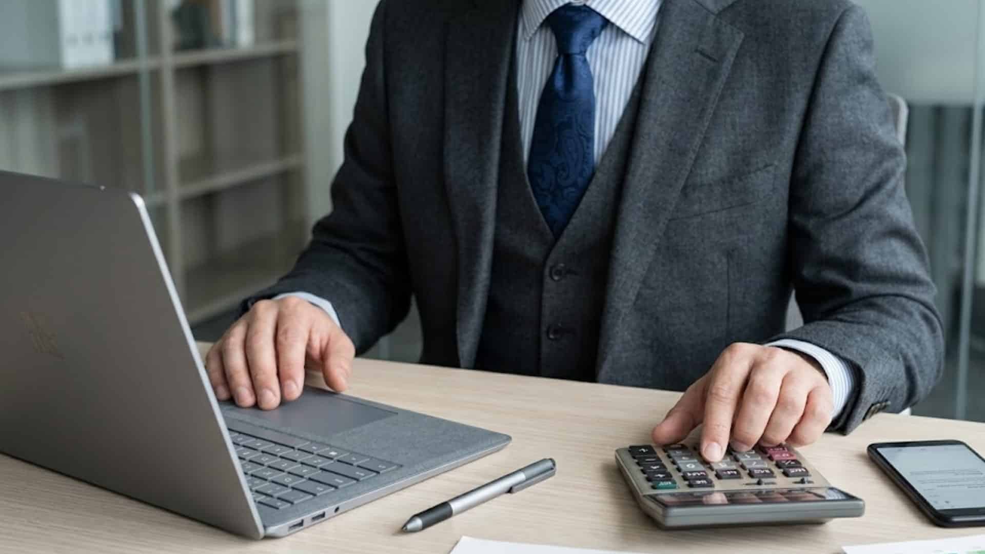 Businessman reviewing bond documents with laptop, calculator, phone, and financial charts on desk