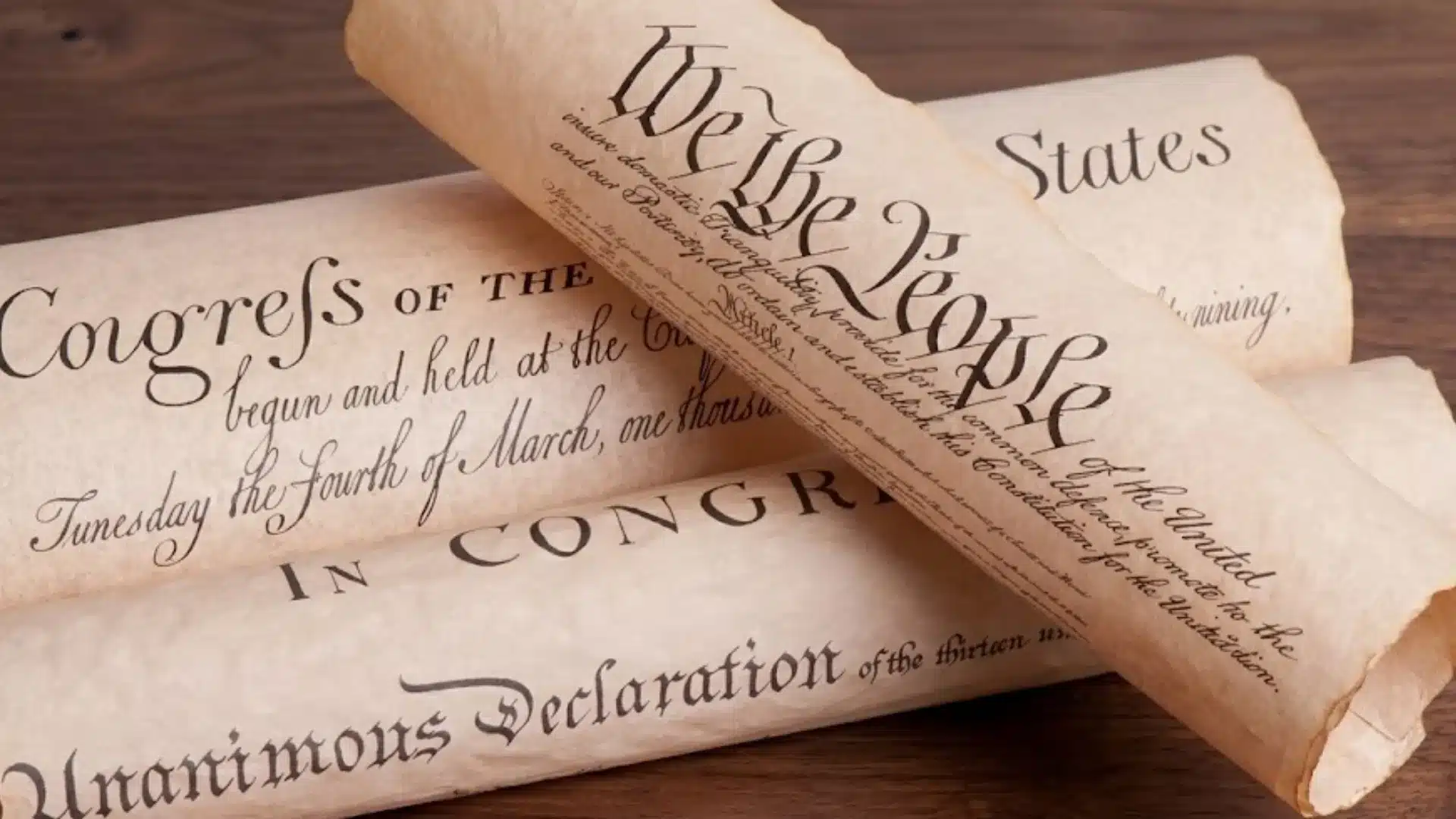 Historic American founding documents on rolled parchment scrolls resting on a wooden table