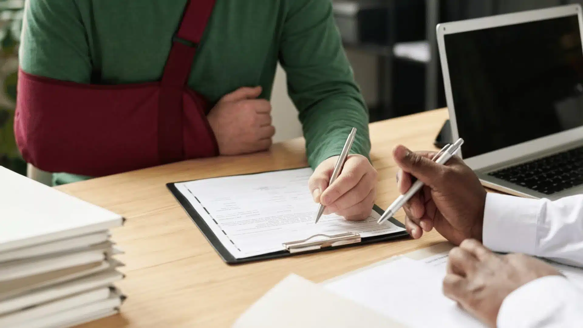 Injured client with arm sling reviewing personal injury claim forms with a lawyer