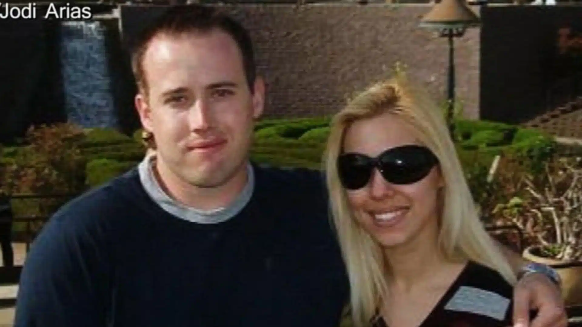 Jodi Arias and Travis Alexander standing together outdoors during their relationship, with Arias wearing sunglasses and Alexander placing his arm around her