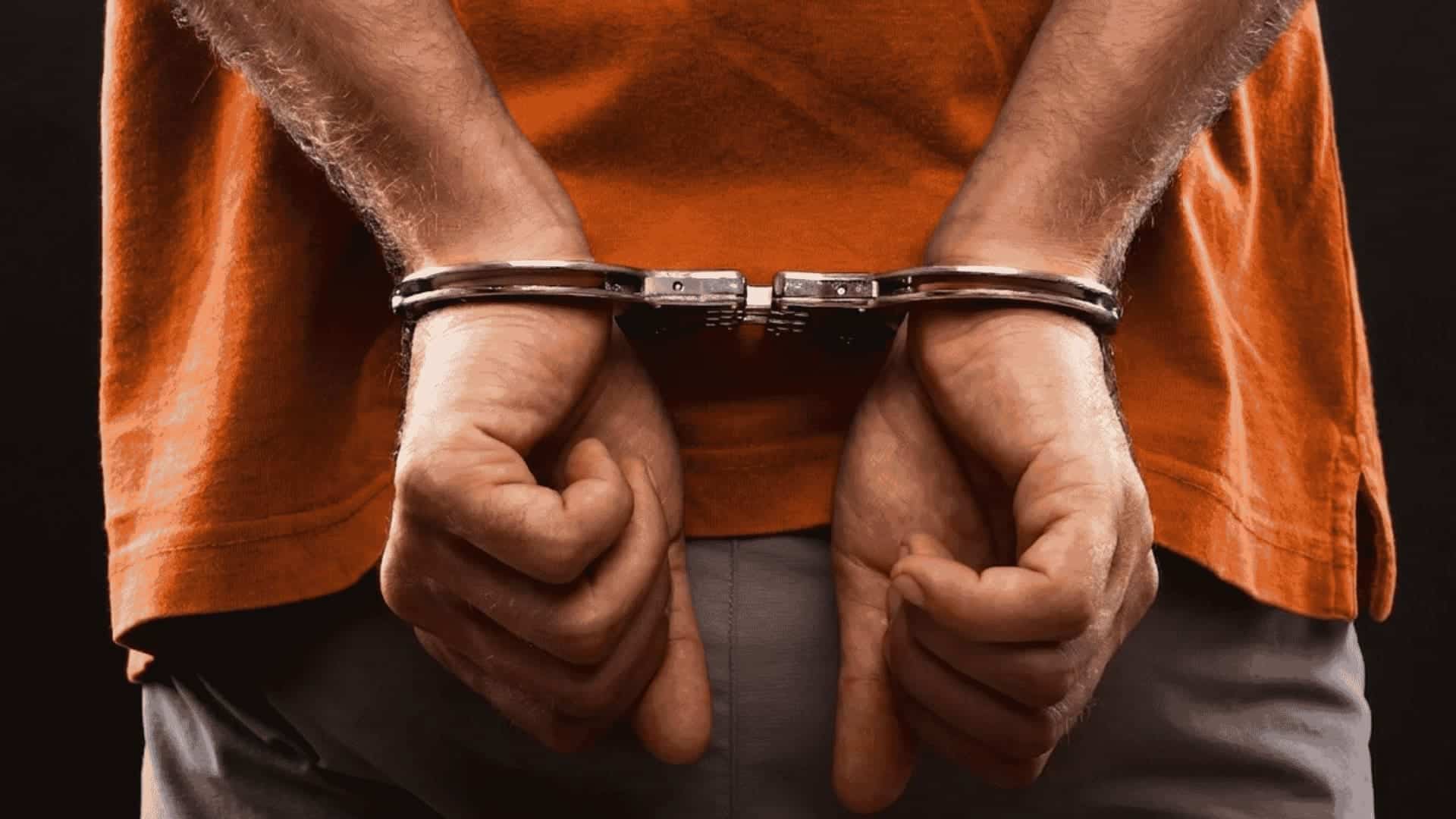 Man in an orange shirt with hands handcuffed behind his back
