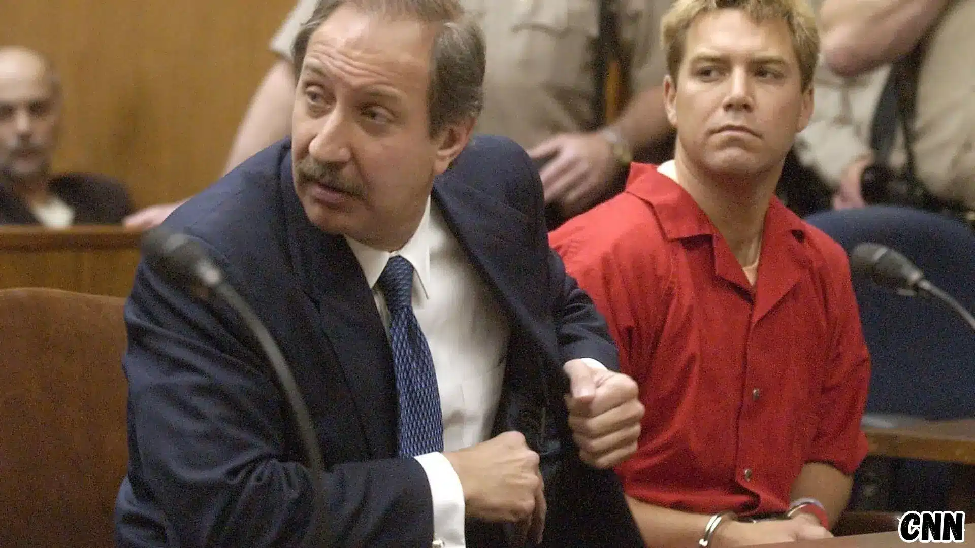 Scott Peterson sits in court beside his attorney during trial proceedings while wearing a red jail uniform and handcuffs
