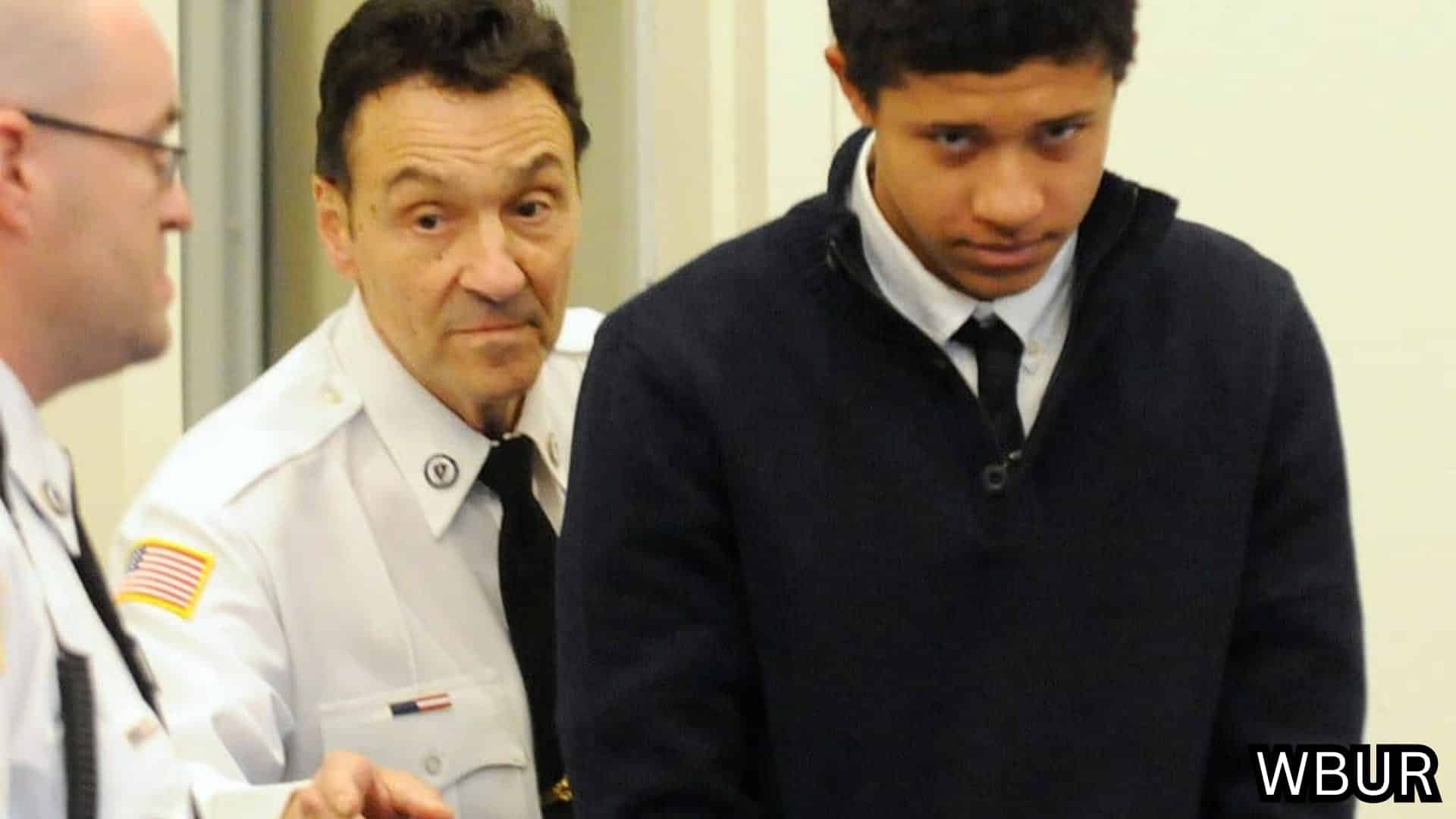 Uniformed officers escort a young man through a courthouse or detention center hallway. (1)