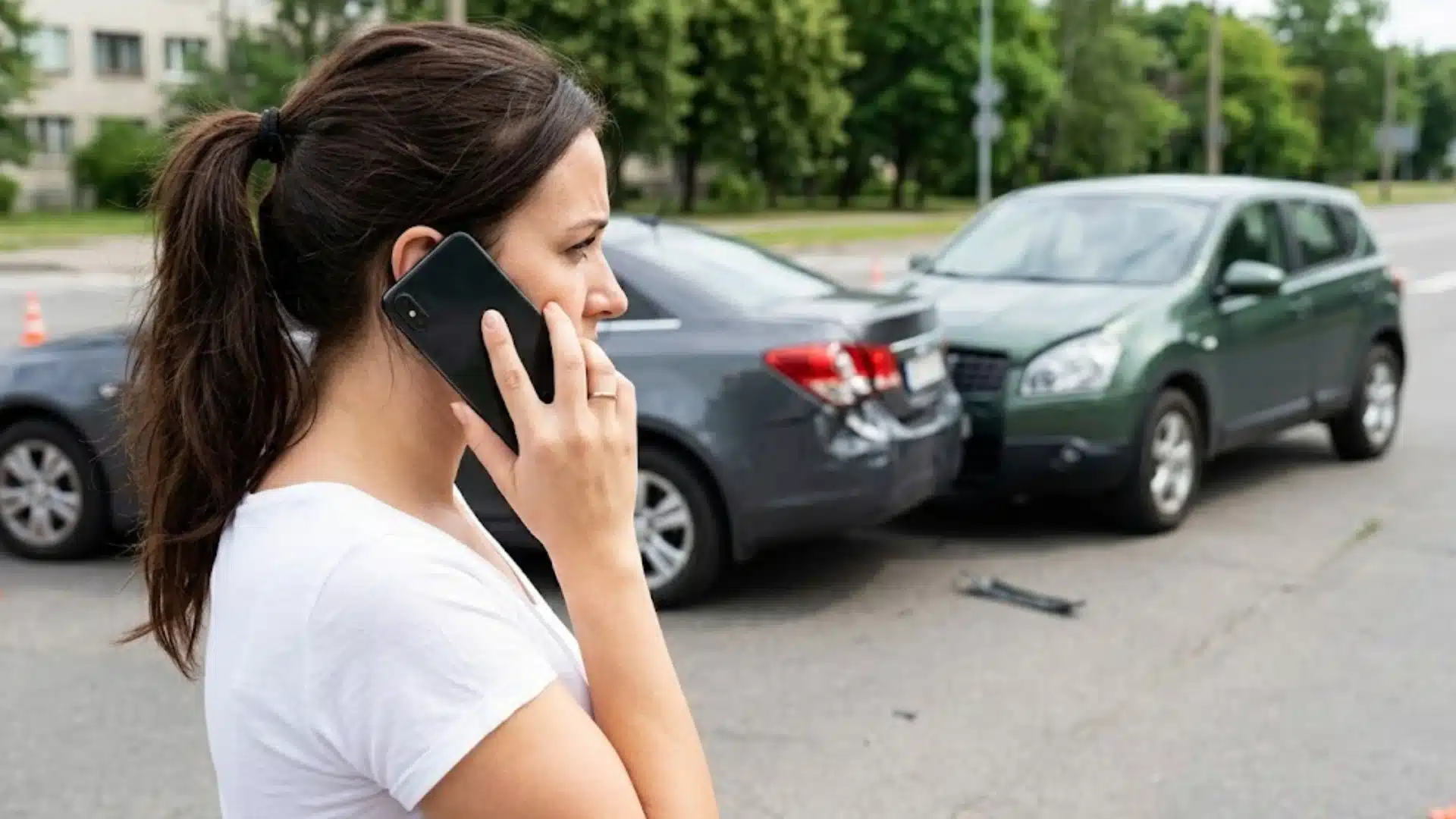Woman calling after a car accident with damaged vehicles behind her on a city road near traffic cones