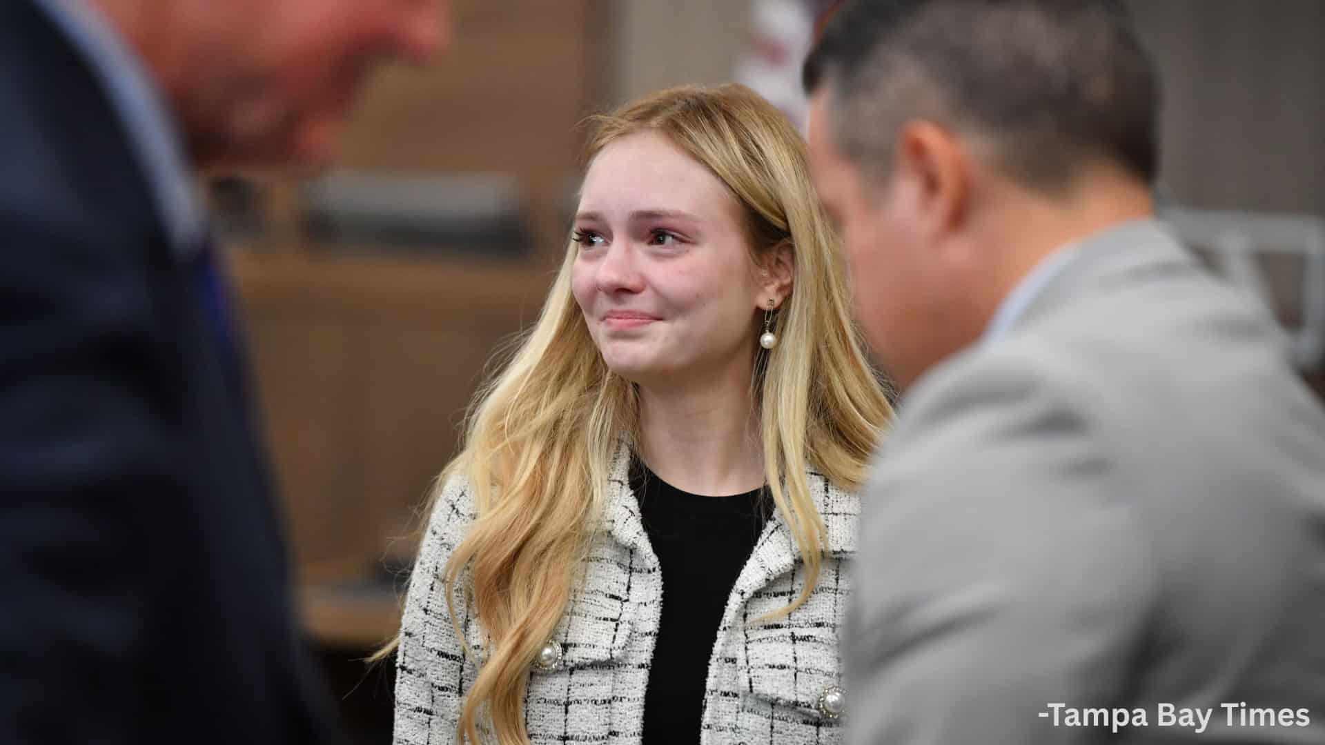 Young woman appearing emotional inside a courtroom while attorneys stand nearby during legal proceedings