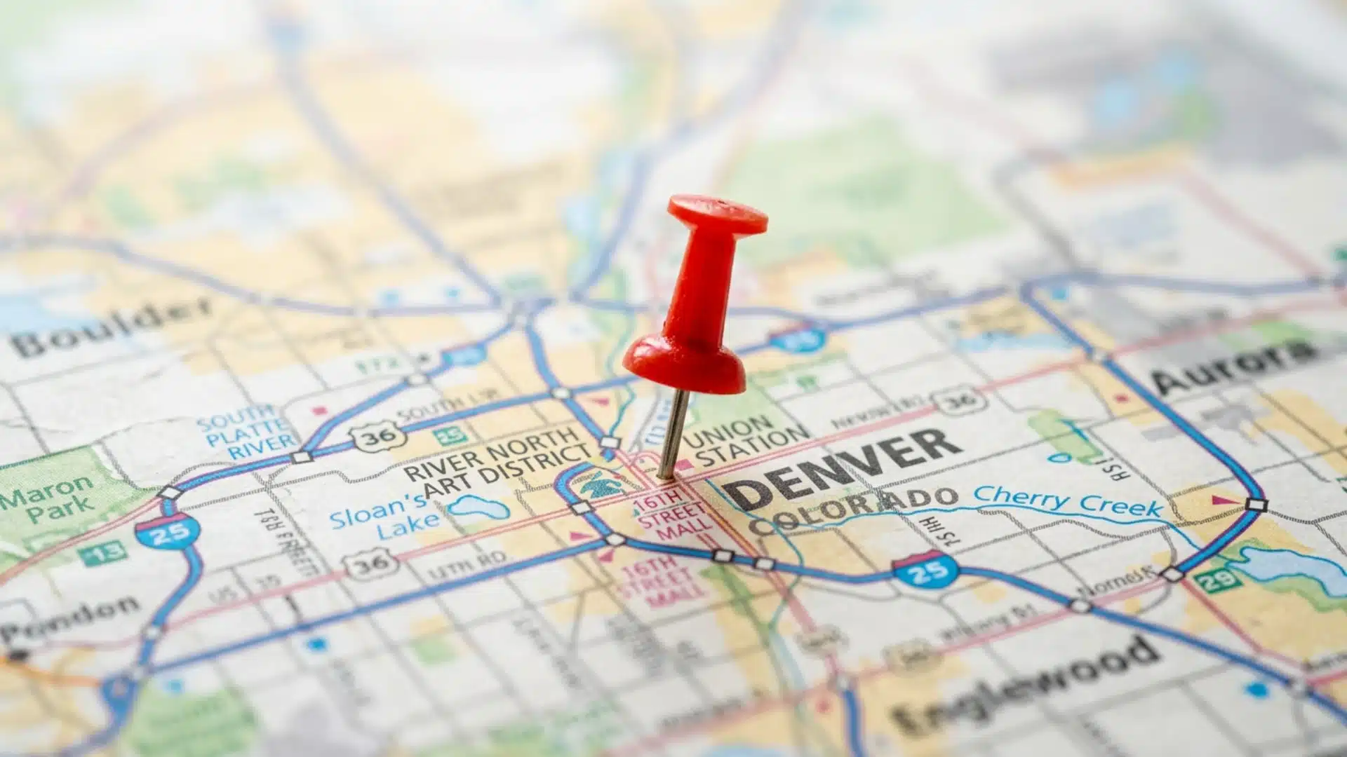 A close-up of a paper map showing Denver, Colorado, with a red pushpin placed near the 16th Street Mall