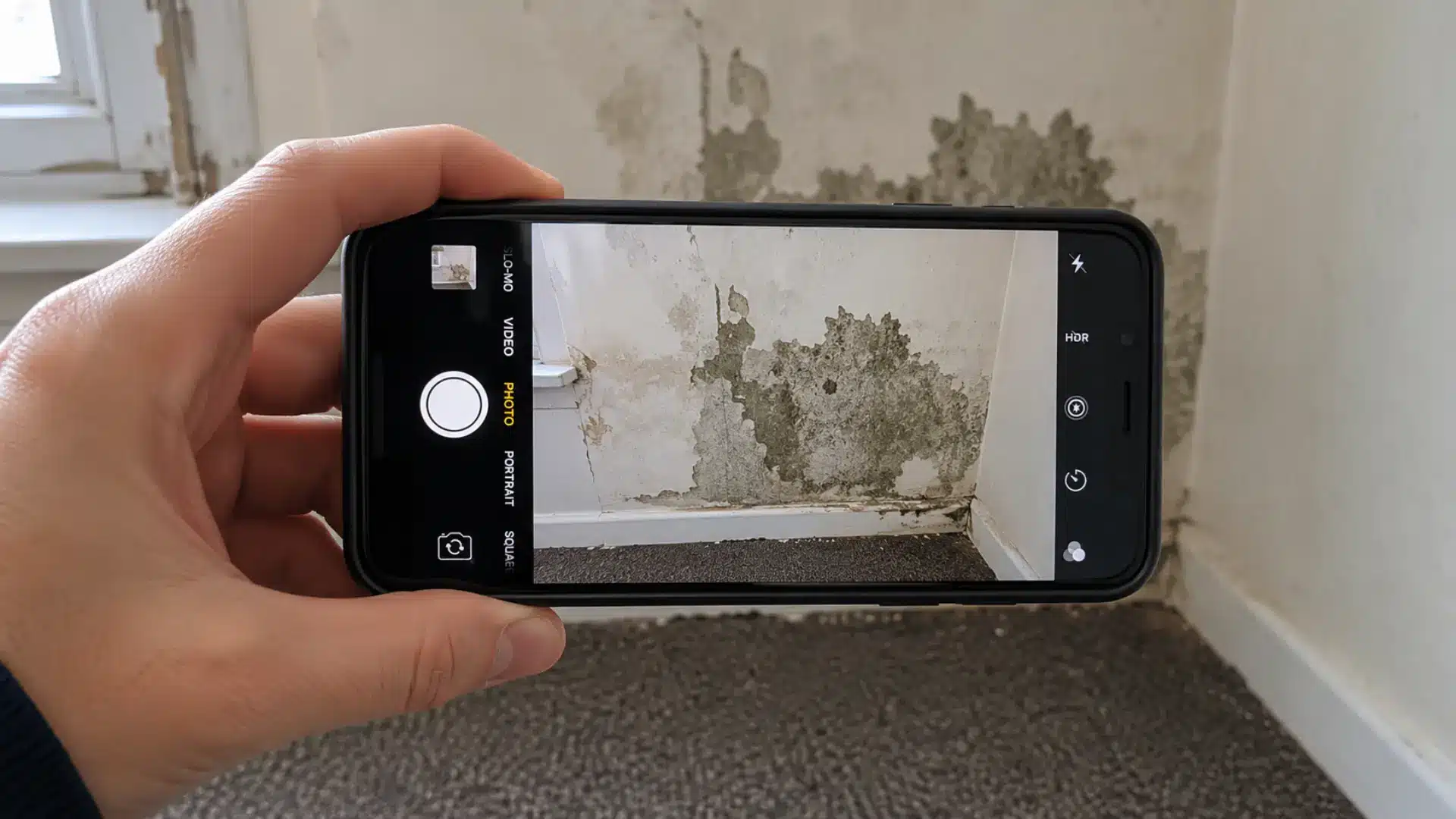 A tenant's hand holding a smartphone photographing water damage and mold