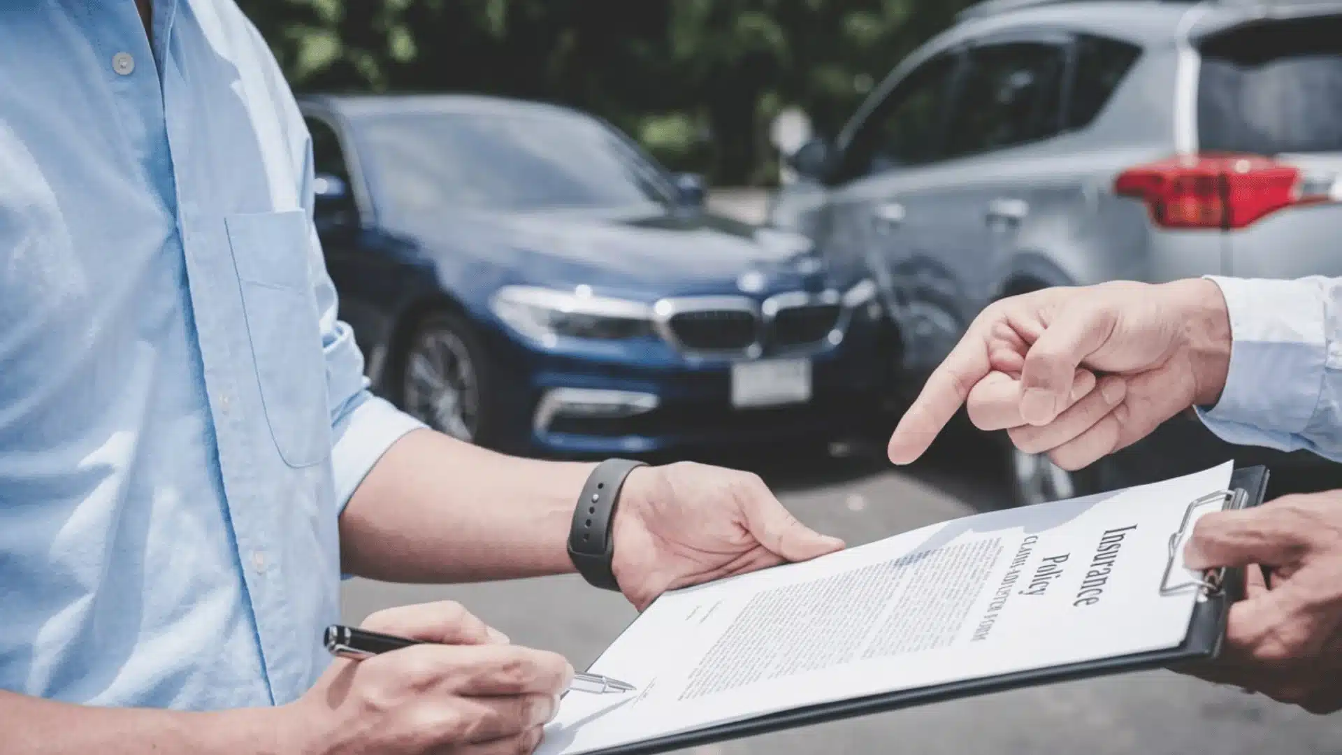 Driver signs insurance claim paperwork after a car accident with damaged vehicles in the background