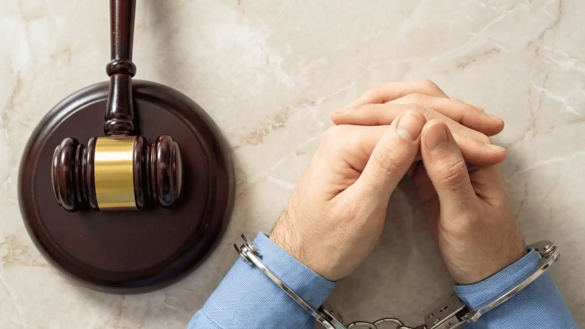 Handcuffed person with clasped hands beside a judge's gavel, representing an assault charge and criminal court proceedings