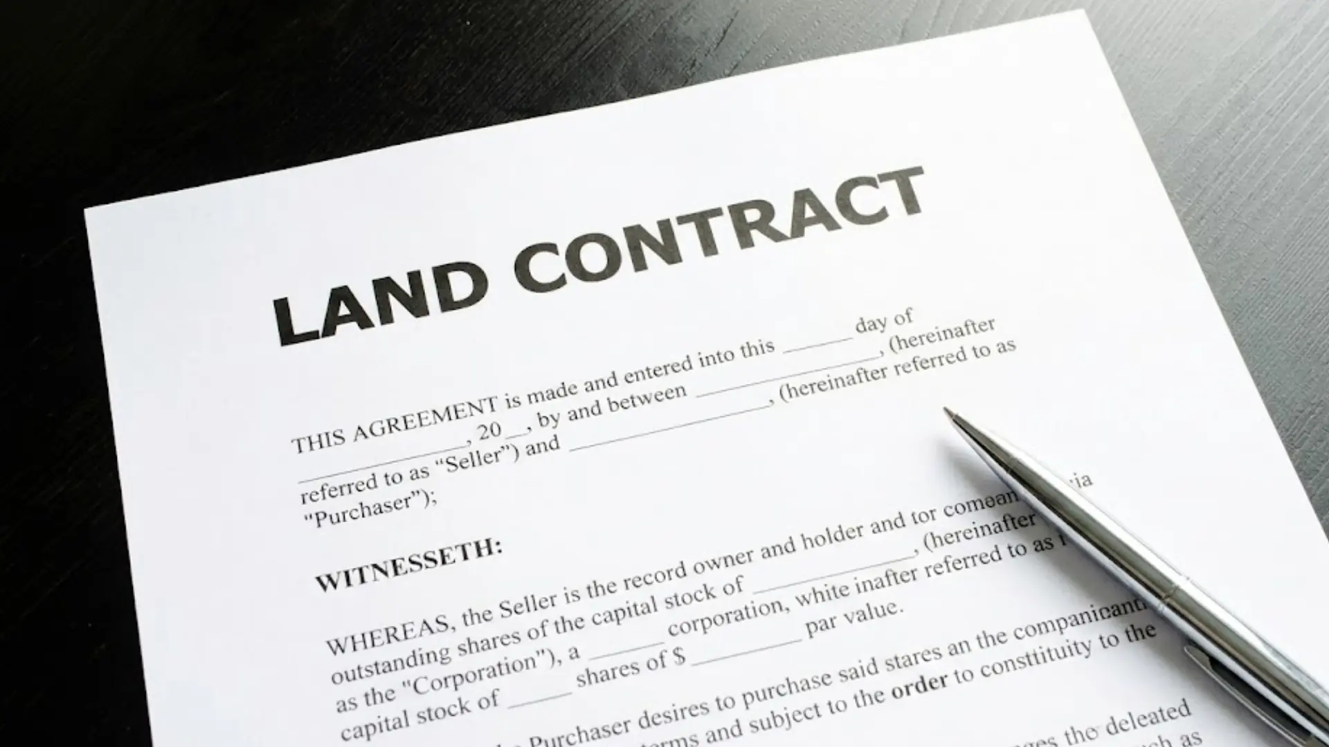Land contract agreement document with a pen placed on top, showing property sale contract details