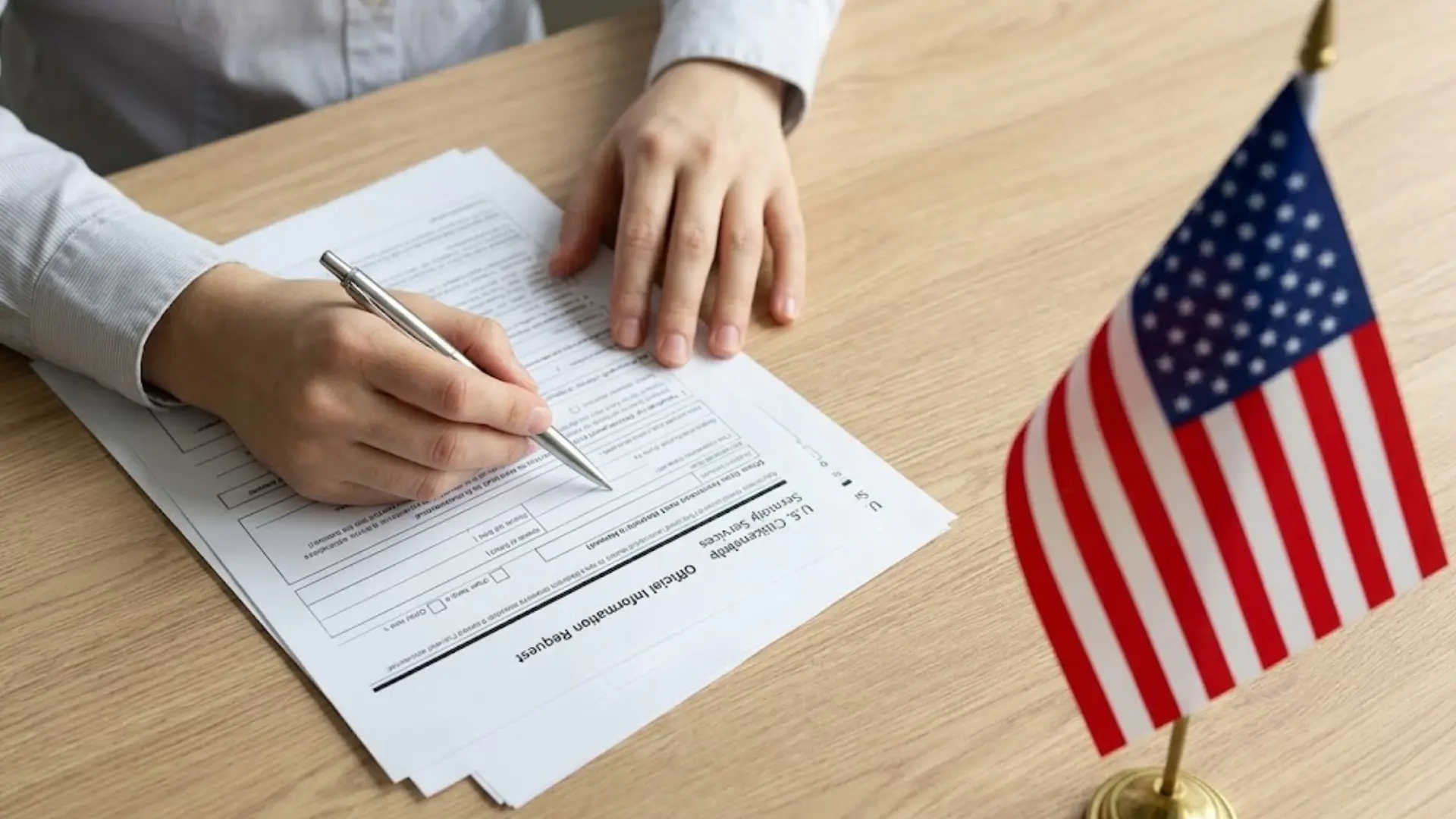 Person filling out a U.S. immigration form beside an American flag on a desk