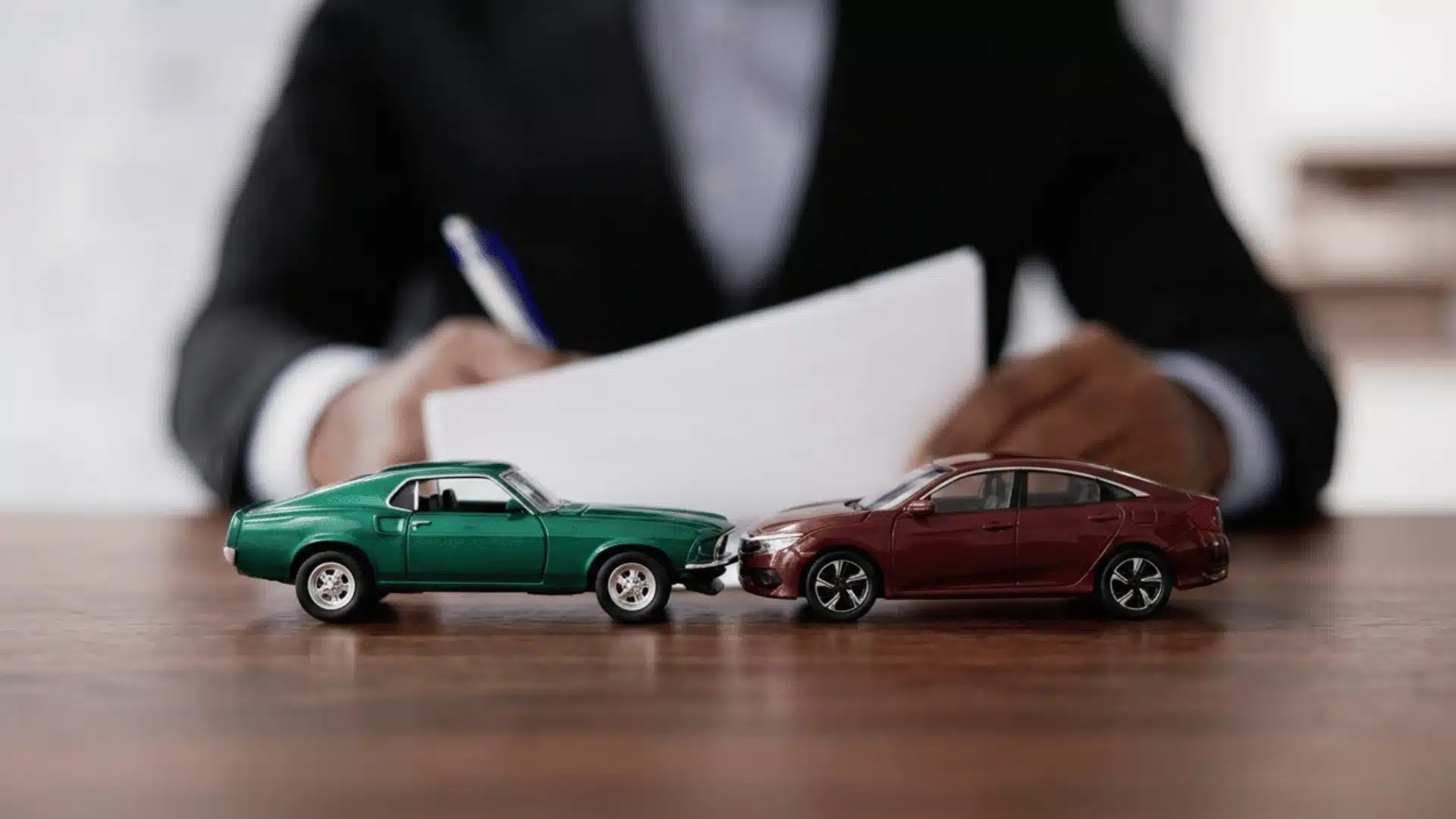 Toy cars in a minor collision with a person reviewing accident paperwork in the background
