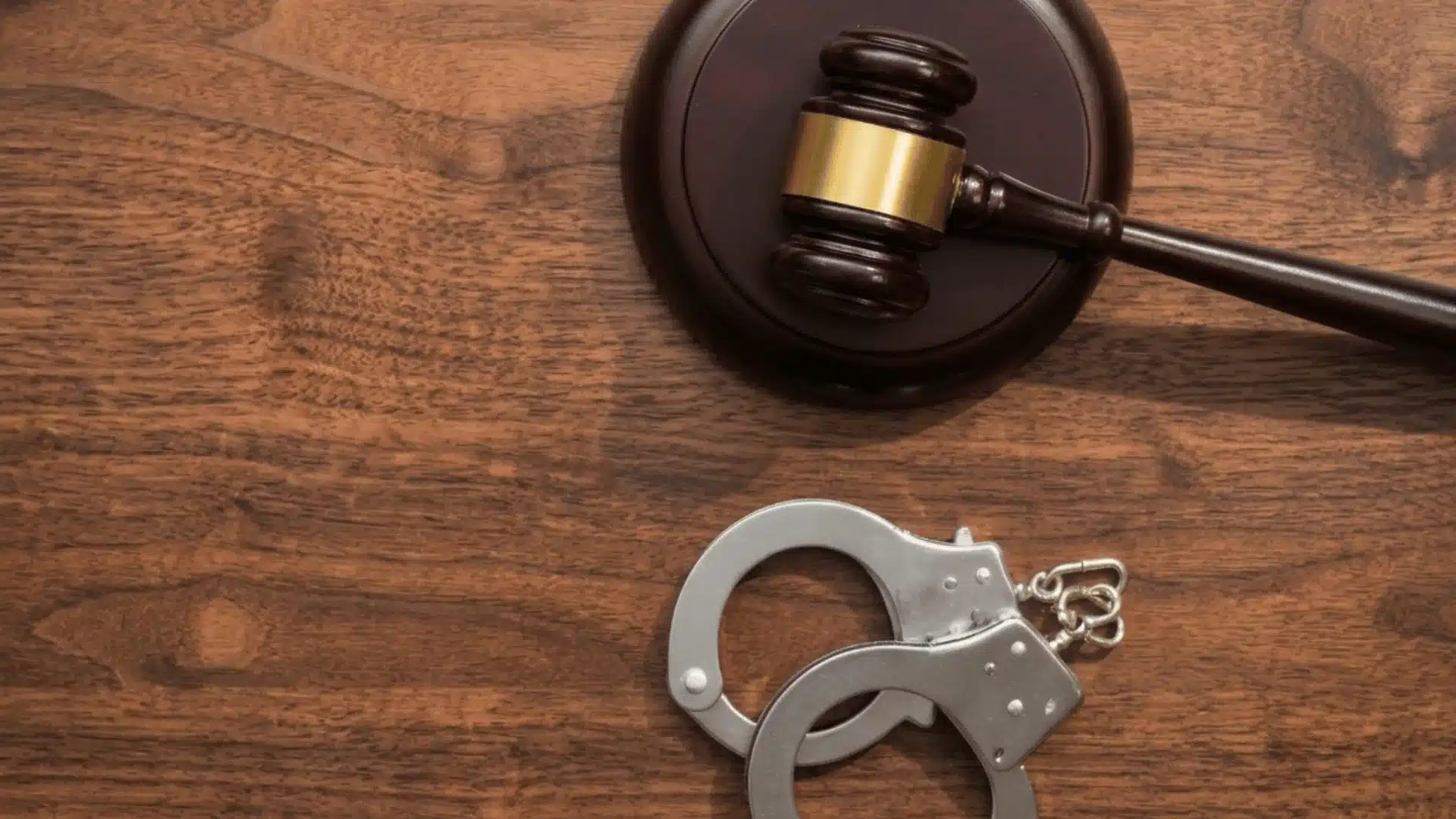 Wooden judge's gavel and silver handcuffs on a wooden table symbolizing criminal law