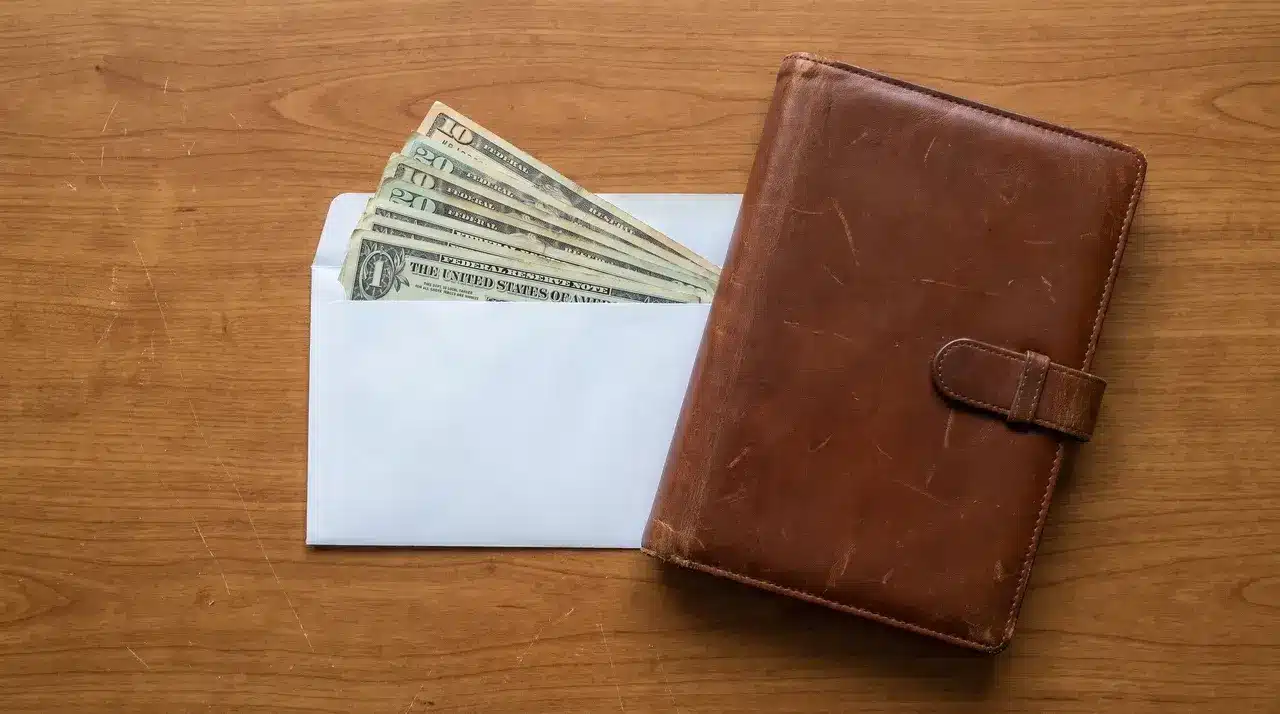 Stack of cash in an envelope beside a closed folder on a desk