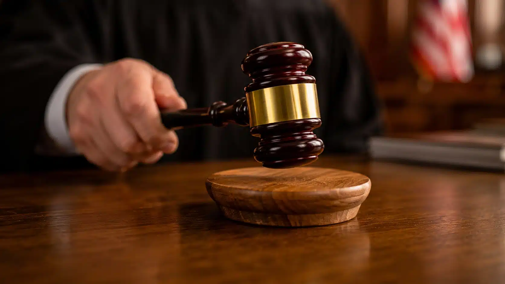 Judge holding a wooden gavel above a sound block in a courtroom, symbolizing legal decisions and the justice system.
