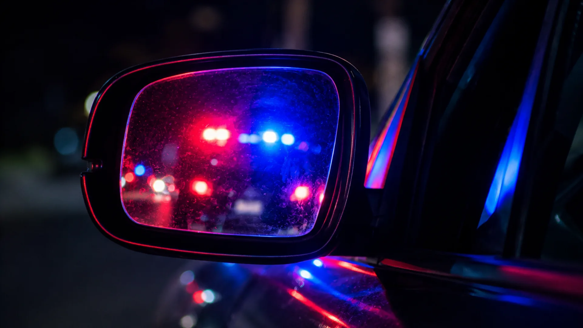 Police lights reflected in a car mirror during a DUI traffic stop at night