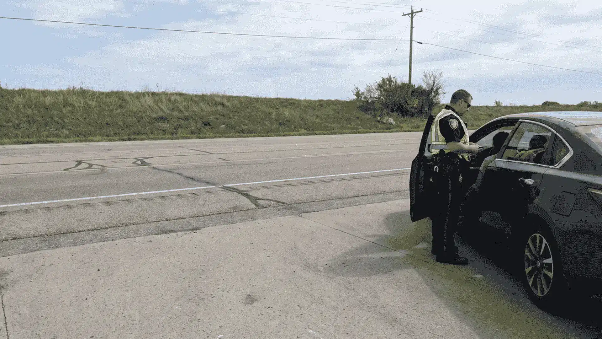 Police officer conducting a brief roadside stop beside a vehicle during a street encounter