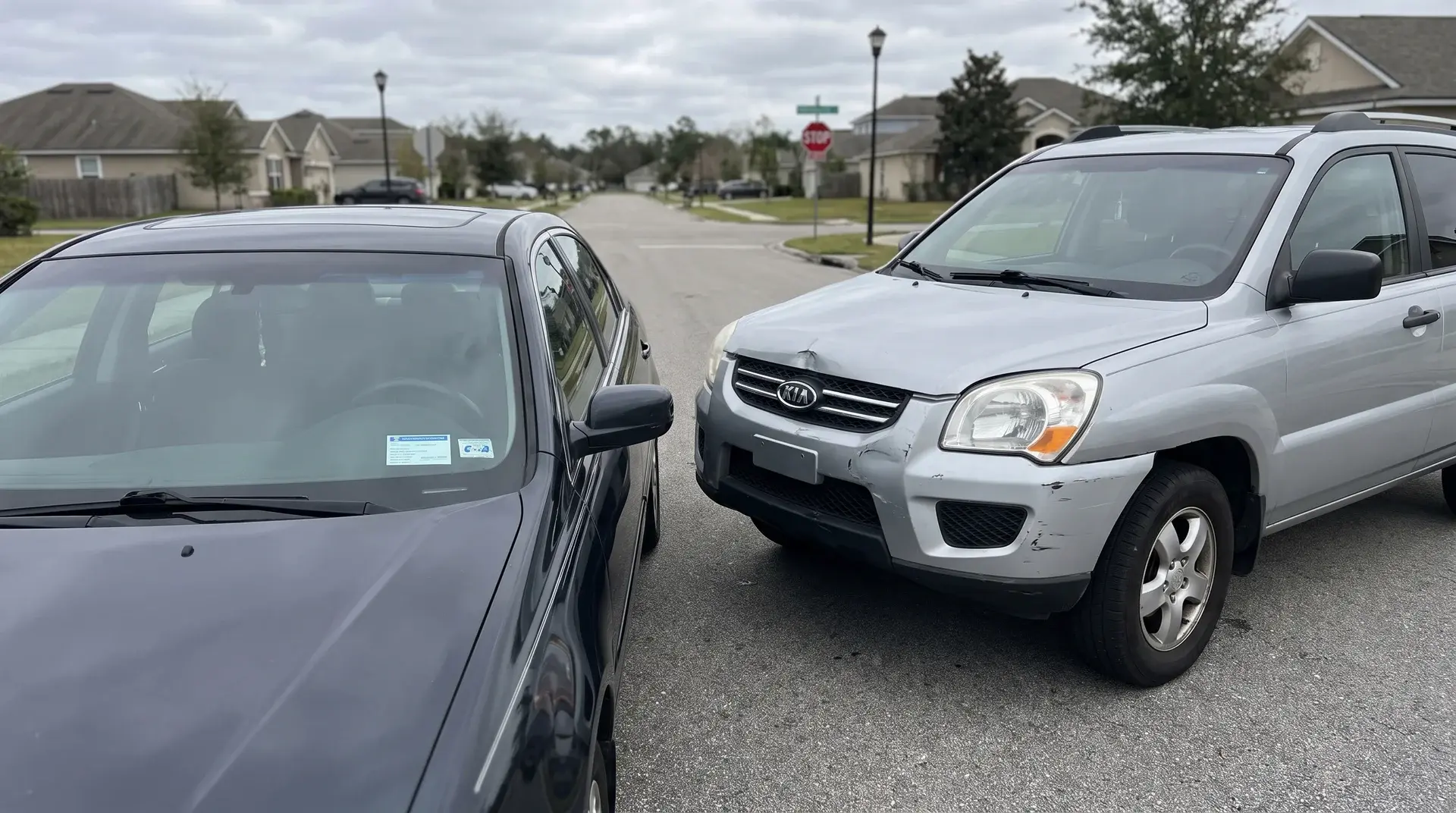 Two cars with front-end contact damage at an intersection, auto insurance card visible on a dashboard