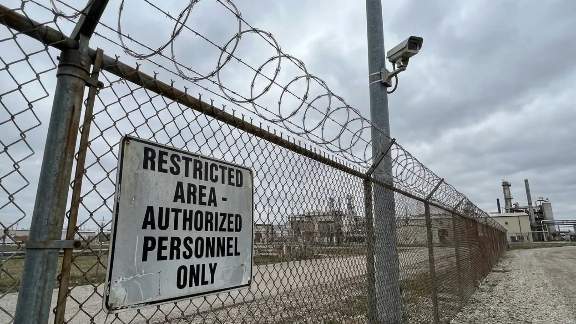 Barbed wire topped security fence with a restricted area sign at an industrial facility